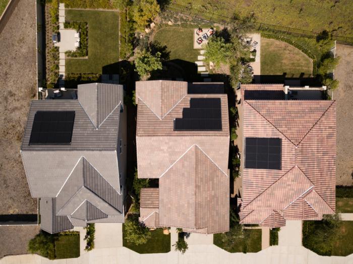 Overhead sky view of three homes with solar panels installed on top of the roofs.