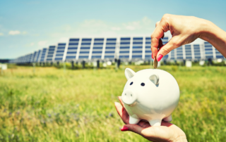 Photo shows a background of multiple solar panels and a person holding a piggy bank with one hand and the other hand putting a coin into the piggy bank symbolizing saving $ with solar