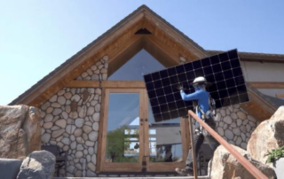 Photo shows solar installation worker holding a solar panel up in front of a home during an installation