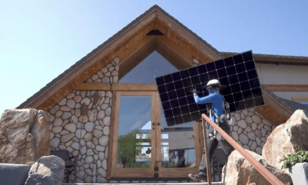 Photo shows solar installation worker holding a solar panel up in front of a home during an installation