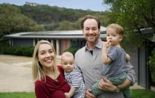 Photo of a family together holding their two children in their arms smiling in front of their home with Evergreen Solar installation.