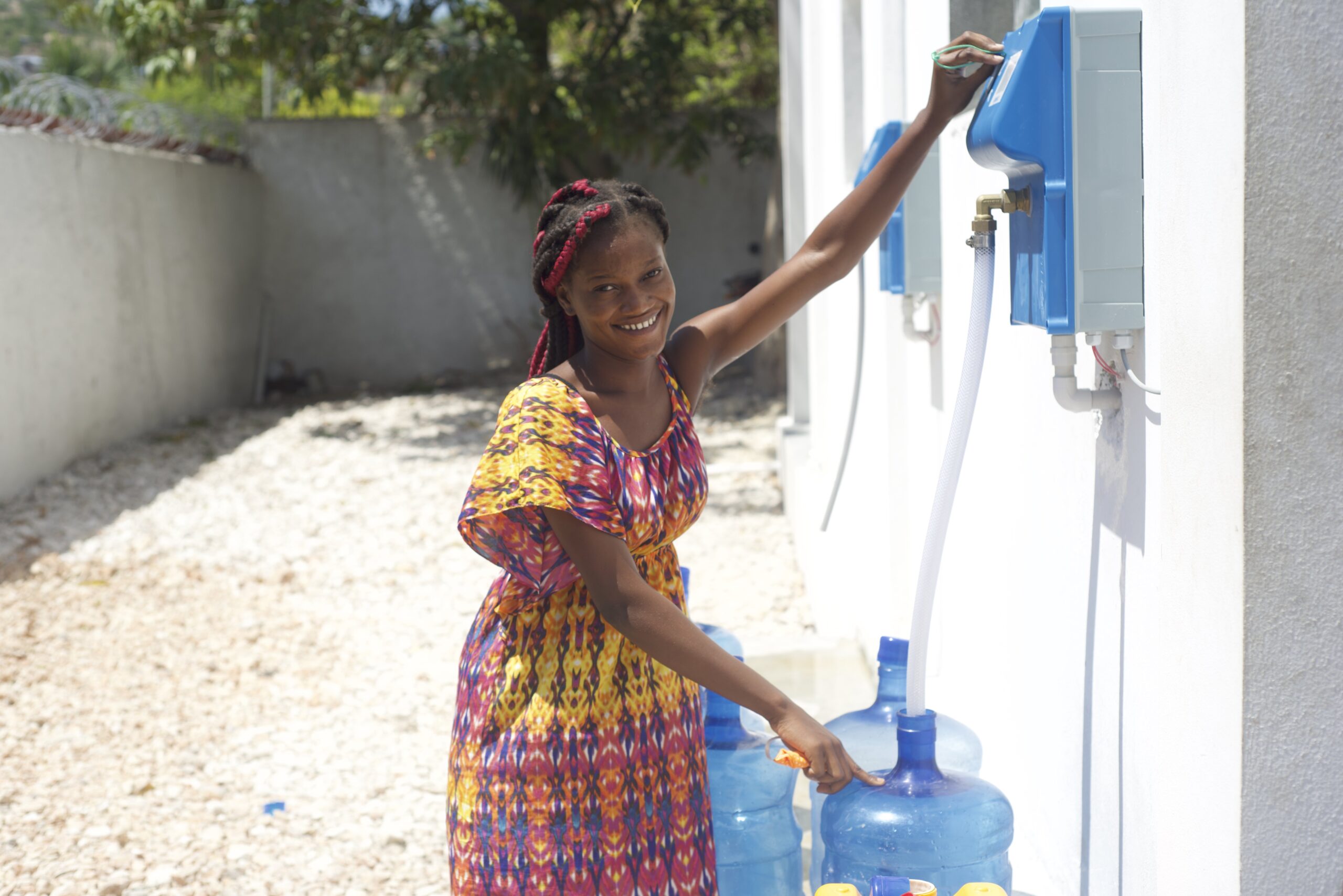A smiling young girl filling up clean drinking water in 5 gallon bottles.